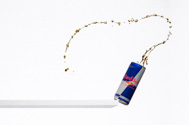 can of Red Bull falling off a shelf with liquid splashing out